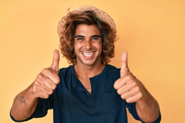 Yazlık şapkalı genç adam elinle olumlu jest yapmayı onaylıyor. Gülümsüyor ve başarı için seviniyor. kazanan jest. 