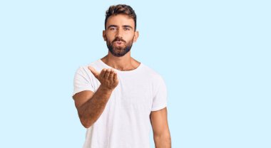 Gündelik beyaz tişört giyen genç İspanyol adam kameraya bakıp havada bir öpücük savuruyor ve güzel ve seksi oluyor. aşk ifadesi. 