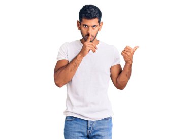 Gündelik kıyafetler giyen genç latin adam sessiz olmak istiyor. Parmakları dudaklarında, elleri yanda. sessizlik ve gizli konsept. 