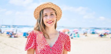 Kumsalda yürürken gülümseyen genç sarışın kadın.