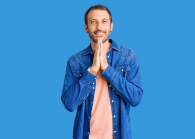 Genç, yakışıklı bir adam, günlük giysiler içinde ellerini birleştirip dua ediyor, af diliyor, gülümsüyor.. 