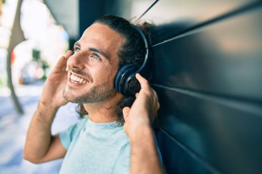 Genç İspanyol gülümseyen adam şehirde kulaklık takarak müzik dinlemekten mutlu oluyor..