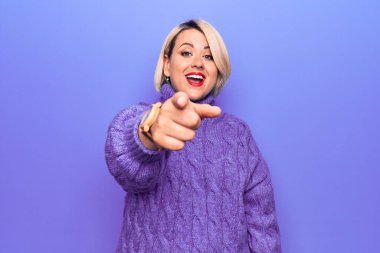 Güzel sarışın ve cüsseli bir kadın mor arka plan üzerine balıkçı yaka kazak giyiyor. Kameraya kızgın ve sinirli olduğunu gösteriyor.