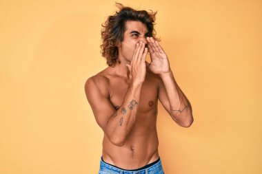 Genç İspanyol adam üstsüz duruyor ve elleri ağzında kızgın bir şekilde bağırıyor. 