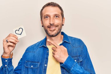 Genç ve yakışıklı bir adam kalbi tutuyor gülümsüyor mutlu eli ve parmağı ile işaret ediyor 