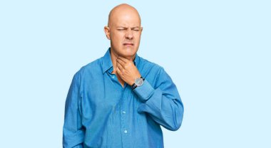 Orta yaşlı kel bir adam günlük giysiler giyiyor. Ağrılı bir boyuna dokunuyor. Grip, mantar ve enfeksiyon yüzünden boğaz ağrısı çekiyor. 