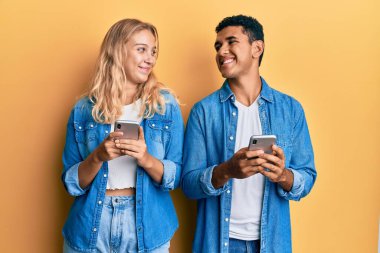 Genç ırklar arası bir çift akıllı telefon kullanıyor gülümsüyor, yan tarafa bakıyor ve şöyle düşünüyor:. 