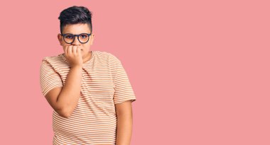 Günlük kıyafetler ve gözlük takan küçük çocuk gergin ve gergin görünüyor. Ağzı tırnak yiyen ellerle. anksiyete. 