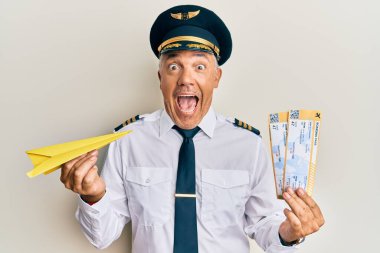 Yakışıklı orta yaşlı yetişkin pilot elinde kağıt uçak ve biniş kartı ile çılgınlığı kutluyor ve şaşırıyor gözleri açık heyecanla bağırıyor.. 