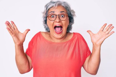 Son sınıf Latin kökenli, gri saçlı, sıradan kıyafetler ve gözlüklü bir kadın çılgın ve başarıyı kutlarken kolları açık, gözleri açık heyecanlı bir şekilde haykırıyor. Kazanan konsept 