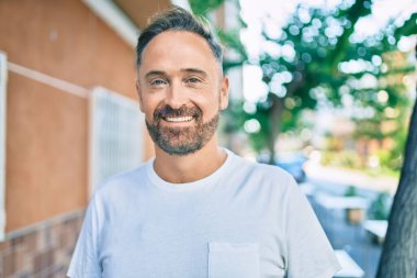 Orta yaşlı, yakışıklı, gülümseyen, mutlu ve şehre bakan bir adam..