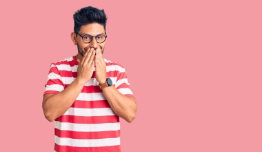 Yakışıklı Latin Amerikalı gündelik kıyafetler ve gözlük takan gülen ve utanan ağzı ellerle, dedikoduyla ve skandalla kaplayan genç adam. 