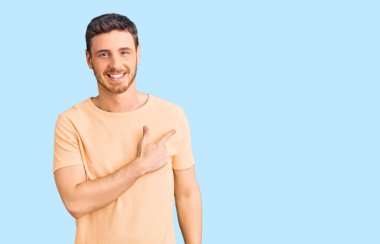 Ayılı yakışıklı genç adam, günlük sarı tişört giyiyor. Neşeli, yüzünde mutlu ve doğal bir ifadeyle, elleri ve parmaklarıyla yüzünü gösteren bir gülümseme var. 