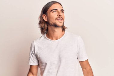 Gündelik giysiler giymiş genç yakışıklı bir adam yüzünde gülümsemeyle yan yana bakıyor, doğal bir ifade. Kendinden emin gülen. 