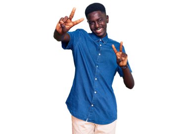 Gündelik giysiler giymiş genç Afro-Amerikan bir adam iki elini de zafer işareti yaparken göstererek gülümsüyor. İki numara.. 