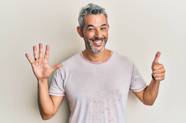 Orta yaşlı, gri saçlı, günlük kıyafetler giyen, altı numaralı parmaklarıyla işaret eden, kendinden emin ve mutlu bir adam.. 