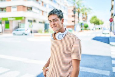 Genç yakışıklı beyaz adam mutlu bir şekilde gülümsüyor. Kulaklık takıyor ve şehirde yürüyor..