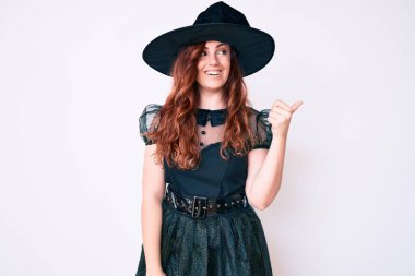 Cadı cadılar bayramı kostümü giyen genç ve güzel bir kadın mutlu yüzle gülümseyen ve başparmağıyla yan tarafı gösteren.. 