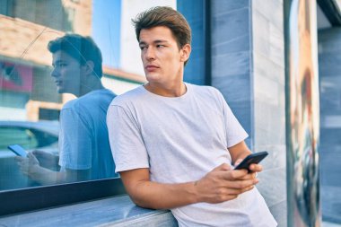 Beyaz adam şehirde akıllı telefon kullanarak mutlu bir şekilde gülümsüyor..