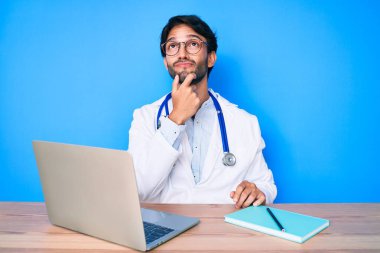 Klinikte çalışan yakışıklı, doktor üniforması giyen, çenesinde parmak olan, şüpheye konsantre olmuş, 