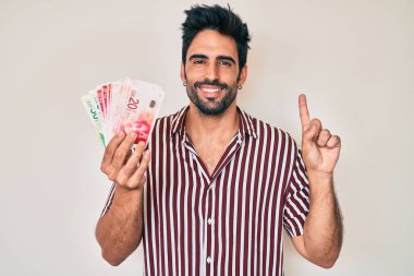 Sakallı yakışıklı İspanyol bir adam İsrail şekelleri tutuyor bir fikir veya soru işareti ile gülümsüyor mutlu bir yüzle, bir numara 