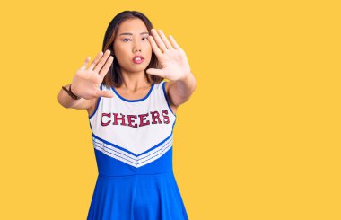 Genç, güzel Çinli kız ponpon kız üniforması giyiyor. El ve parmakları kullanarak çerçeve yapıyor. Kamera bakış açısı. 