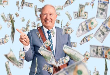 Kıdemli yakışıklı, gri saçlı takım elbiseli ve çantalı adam gülümsüyor mutlu bir şekilde elini ve parmağını yana doğru gösteriyor.