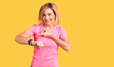 Spor kıyafetleri giyen genç sarışın kadın acele edip saati, sabırsızlığı ve gecikmeye kızmayı işaret ediyor. 