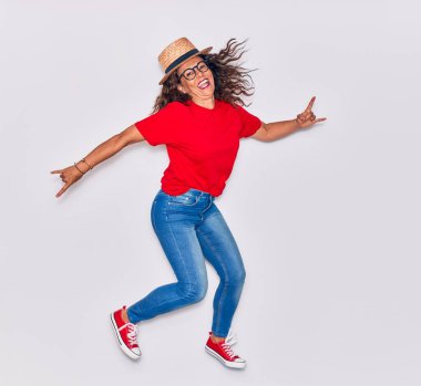 Orta yaşlı, güzel İspanyol bir kadın, sıradan kıyafetler giyiyor ve mutlu bir şekilde gülümsüyor. Beyaz arka planda gülümseyerek atlamak