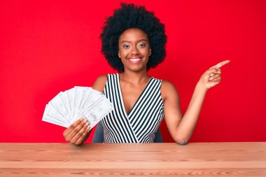 Genç Afro-Amerikalı kadın elinde dolarlarla mutlu bir şekilde gülümsüyor. 