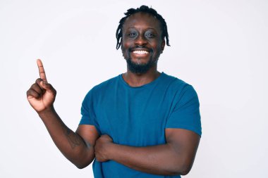 Saçları örgülü, yüzünde kocaman bir gülümseme olan, elleri ve parmaklarıyla kameraya bakan Afro-Amerikan genç bir adam.. 