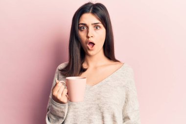 Genç ve güzel bir kız kahve fincanı içiyor korkmuş ve ağzı açık şaşırmış bir şekilde şaşkınlık içinde, inançsız bir yüz. 