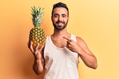 Ananas tutan genç İspanyol adam mutlu bir şekilde elini ve parmağını gösterdi. 