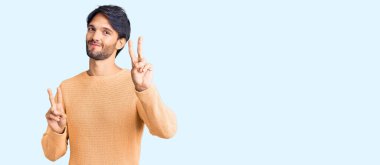 Yakışıklı İspanyol kazaklı adam kameraya bakıp zafer işareti yaparken gülümsüyor. İki numara.. 