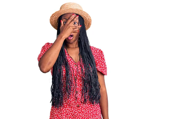 夏の帽子をかぶった若いアフリカ系アメリカ人女性が手で顔と目を覆い 恥ずかしい表情で指を通して見る — ストック写真