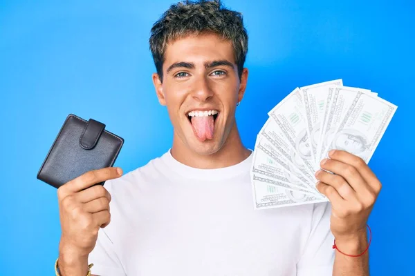 Joven Hombre Guapo Sosteniendo Billetera Billetes Dólares Sacando Lengua Feliz —  Fotos de Stock