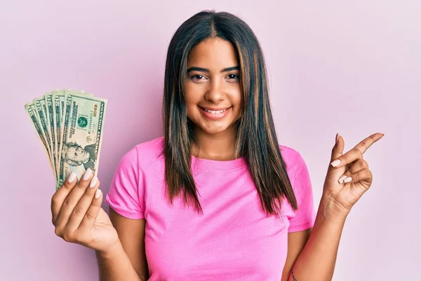 Mladá Latinská Dívka Drží Dolary Úsměvem Šťastný Ukazuje Rukou Prstem — Stock fotografie