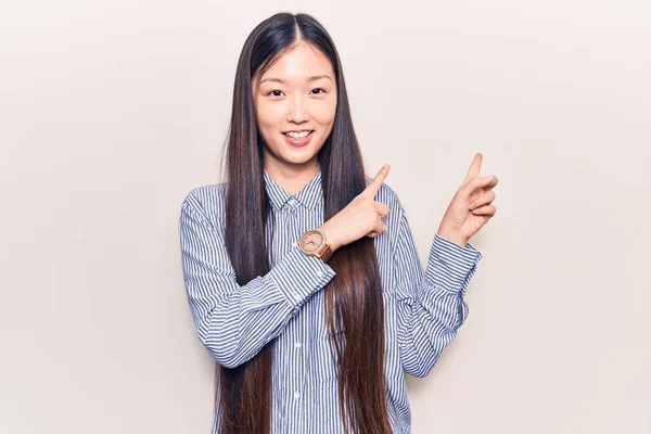 年轻美丽的中国女人 身穿休闲条纹衬衫 面带微笑 看着相机 用双手和手指指向旁边 — 图库照片