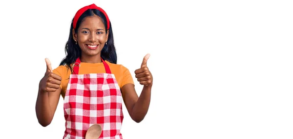 身穿专业烘焙围裙的印度女孩成功地手握双手做着积极的手势 微笑着竖起大拇指 喜形于色 快乐的表达和胜利的姿态 — 图库照片
