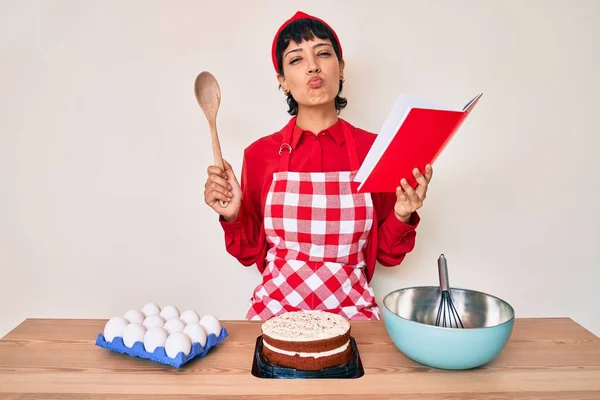 Piękna Brunetka Kobieta Gotowanie Ciasto Czytanie Książki Przepisy Patrząc Aparat — Zdjęcie stockowe