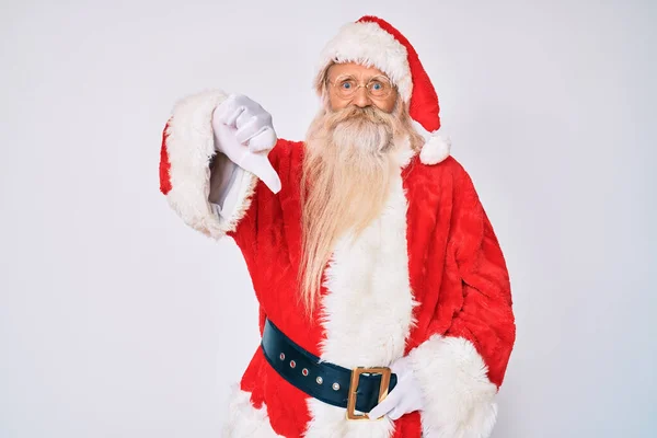 Old senior man with grey hair and long beard wearing santa claus costume with suspenders looking unhappy and angry showing rejection and negative with thumbs down gesture. bad expression.