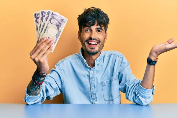 Joven Hispano Sosteniendo Billetes Yen Japoneses Sentado Mesa Celebrando Logro —  Fotos de Stock