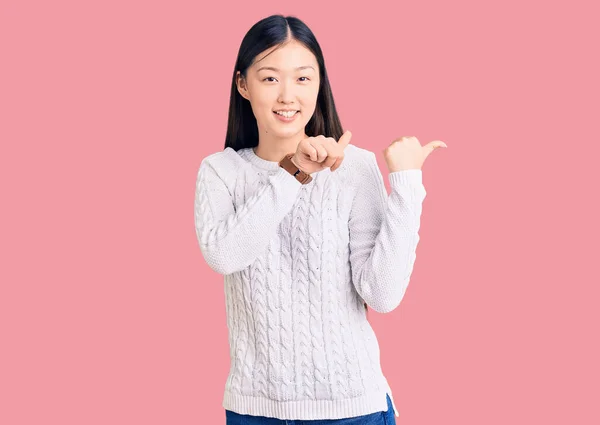 若い美しい中国の女性を着てカジュアルなセーターを手と親指で後ろを指して 自信を笑顔 — ストック写真