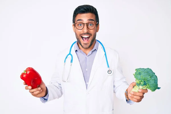 Jovem Hispânico Vestindo Estetoscópio Médico Segurando Pimenta Vermelha Brócolis Sorrindo — Fotografia de Stock