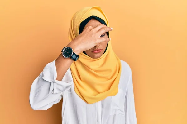 伝統的なイスラムのヒジャーブスカーフを身に着けている若いブルネットのアラブの女性は 鼻と目をこすり疲れや頭痛を感じて疲れている ストレスとフラストレーションの概念 — ストック写真