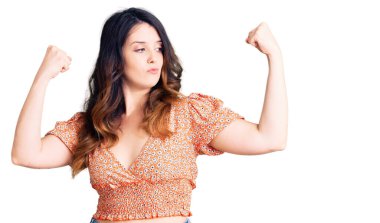 Güzel, genç, esmer, sıradan kıyafetler giyen, gururla gülümseyen kol kaslarını gösteren bir kadın. fitness konsepti. 