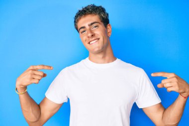 Genç, yakışıklı, günlük beyaz tişört giyen, kendine güvenen, gülümseyen, kendini gururlu ve mutlu gösteren bir adam.. 