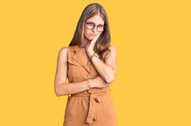 Genç, güzel, sarışın bir kadın. Günlük kıyafetler ve gözlük takıyor. Depresyondan sıkılmış ve yorgun görünüyor.. 