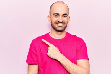 Genç, yakışıklı, kel bir adam, günlük tişört giyiyor. Gülümsüyor, eli ve parmağı yana doğru uzanıyor. 