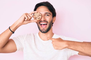 Yakışıklı İspanyol bir adam elinde kurabiyeyle gülümseyen mutlu ve gururlu birini işaret ediyor. 